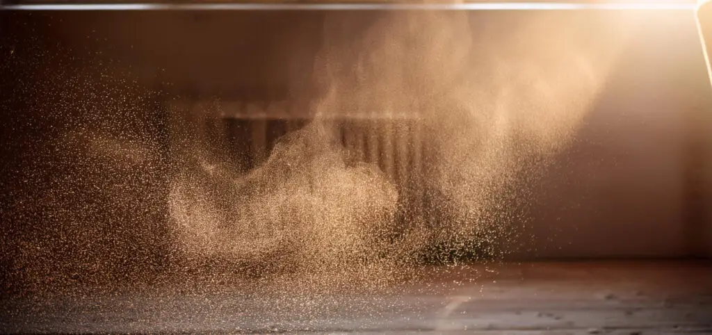 A beam of sunlight illuminates particles of dust floating in the air above a surface indoors.